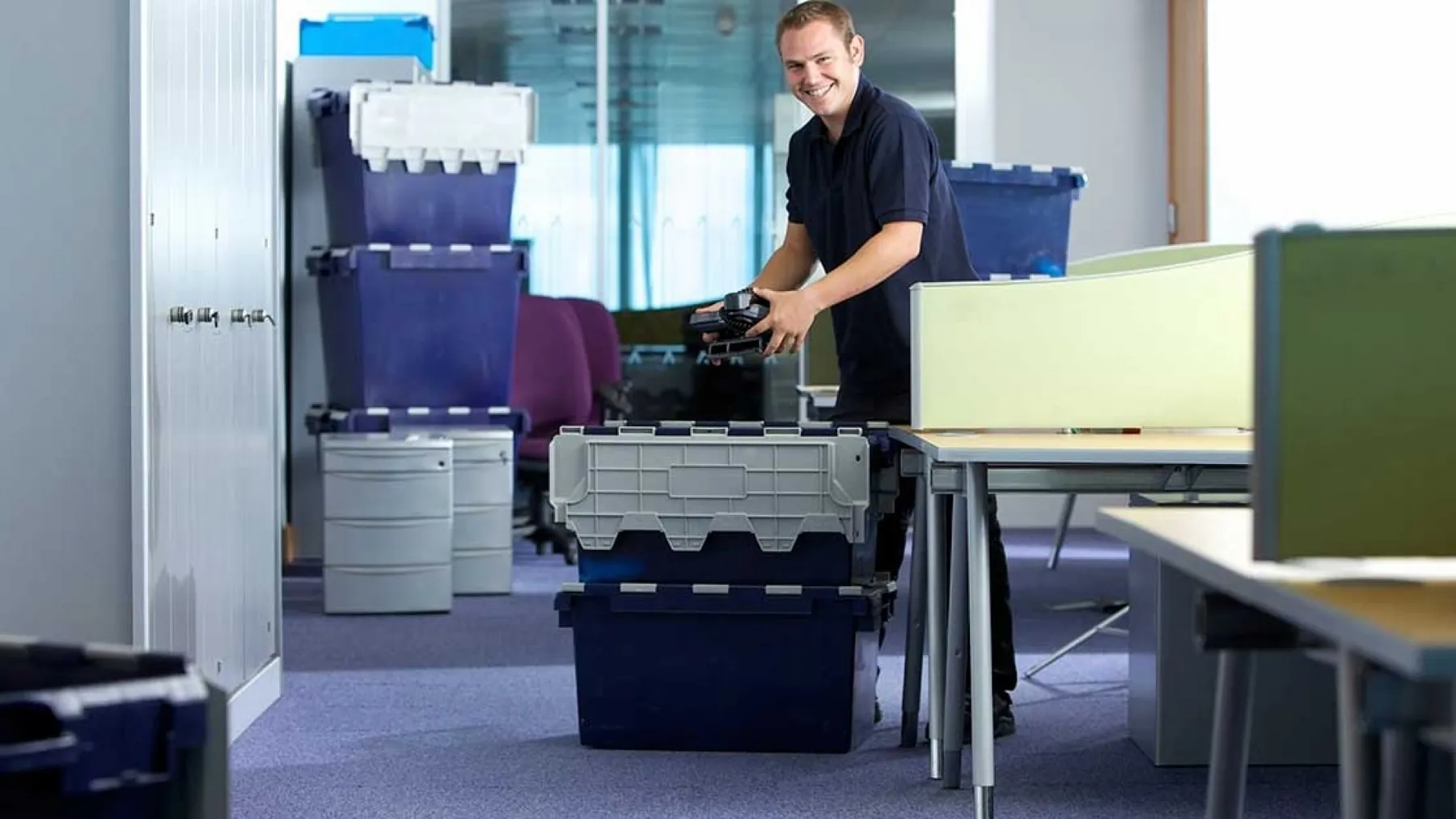Worker packing plastic bins and files in an office during a commercial move