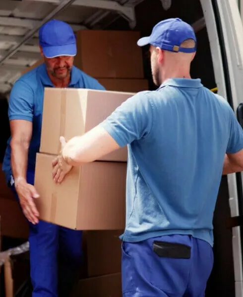 Two movers in blue shirts and caps carrying boxes out of a van