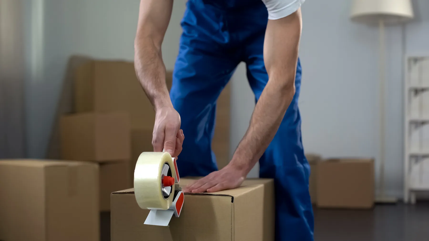 Mover in blue overalls taping a cardboard box shut